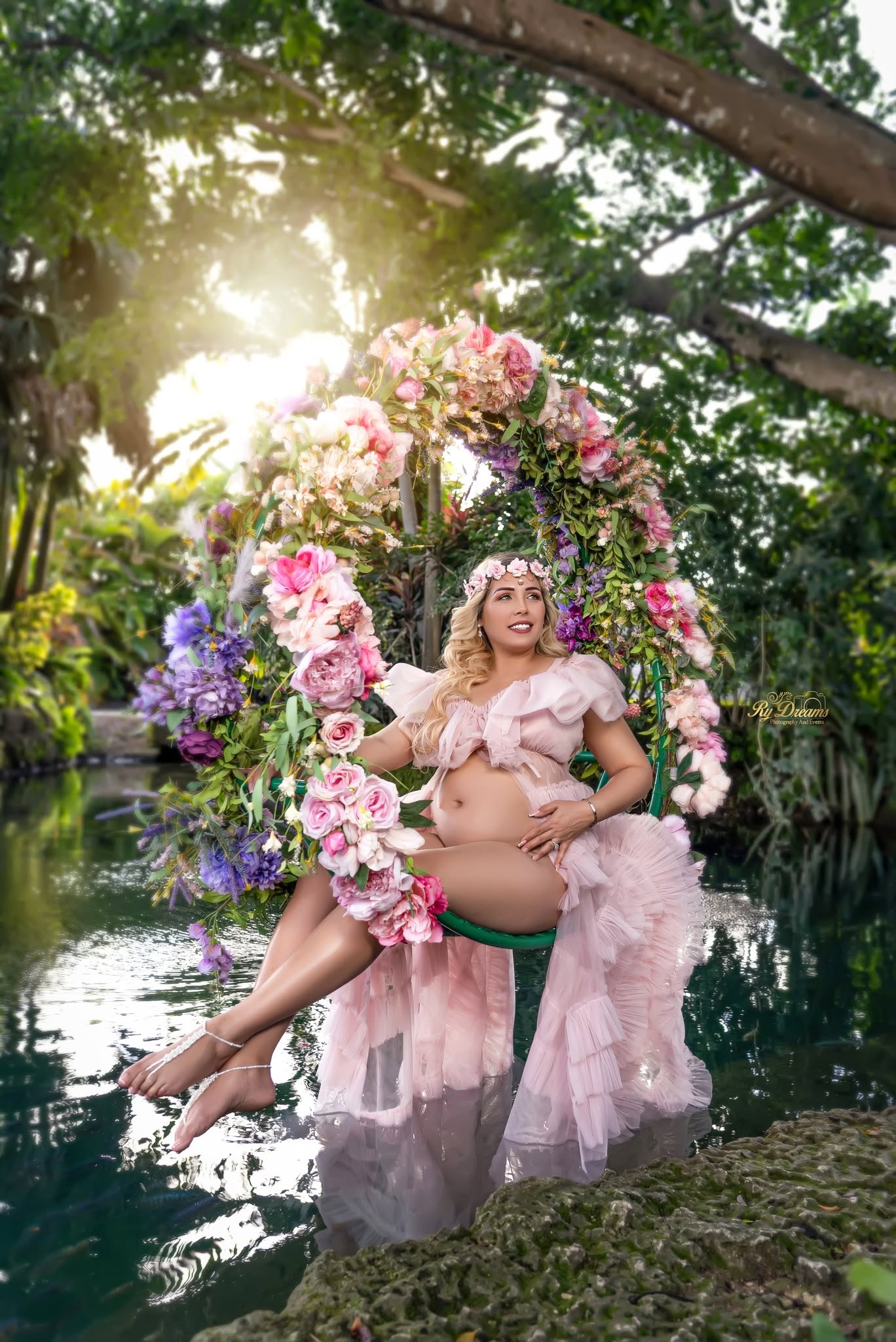 Mamá embarazada en columpio floral junto al agua