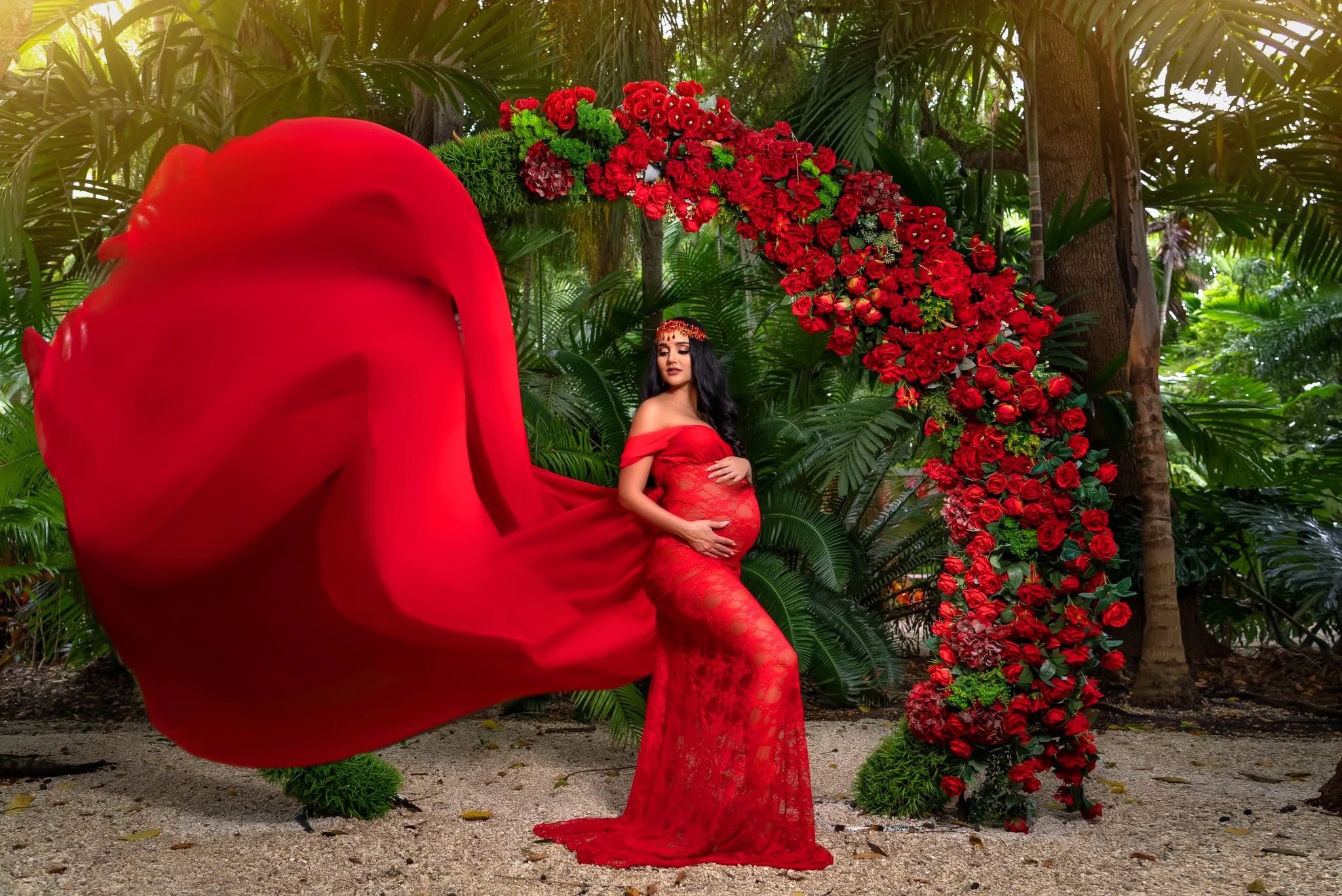 Maternidad en jardín tropical con vestido rojo y arco floral