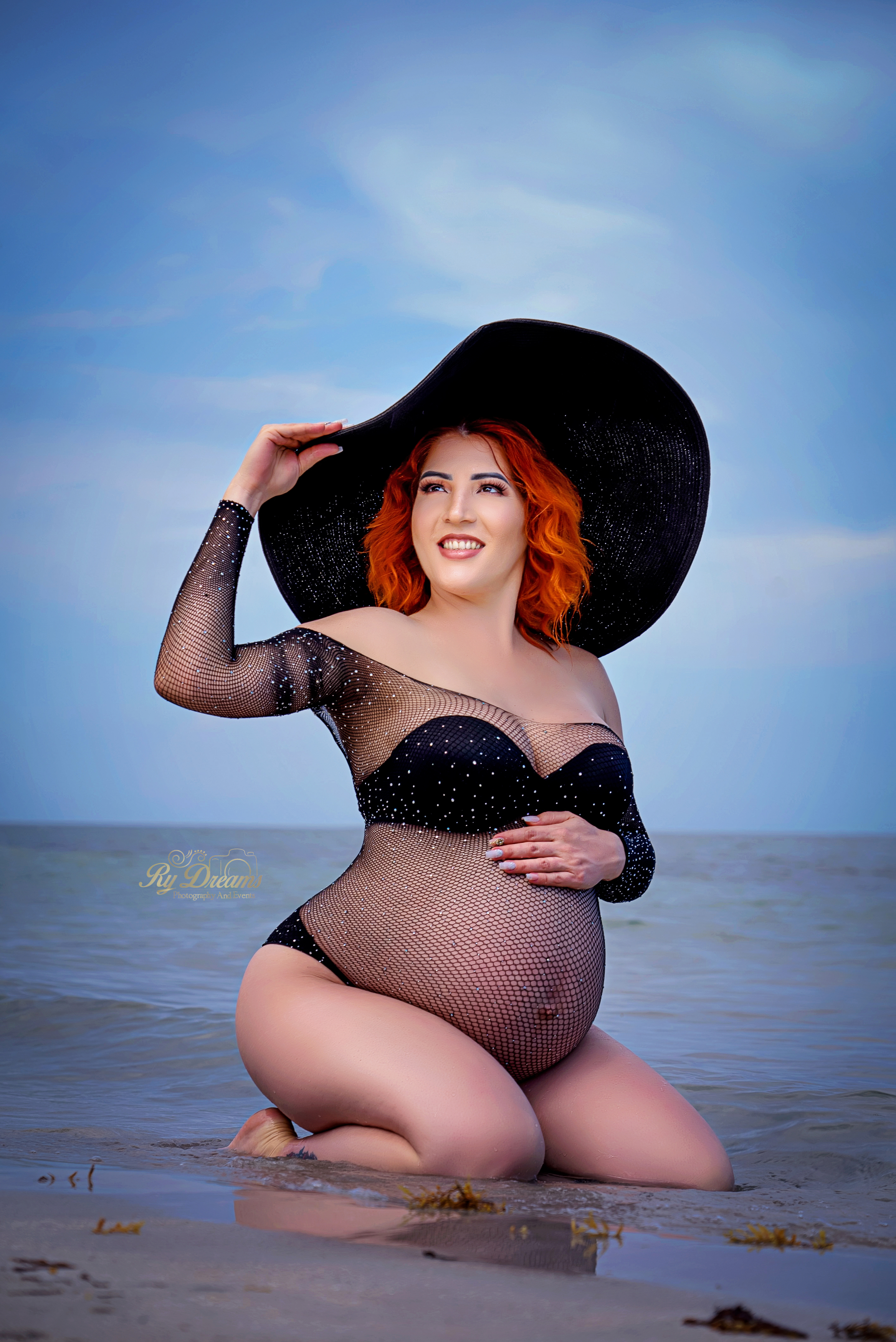Retrato de maternidad en la playa con sombrero negro